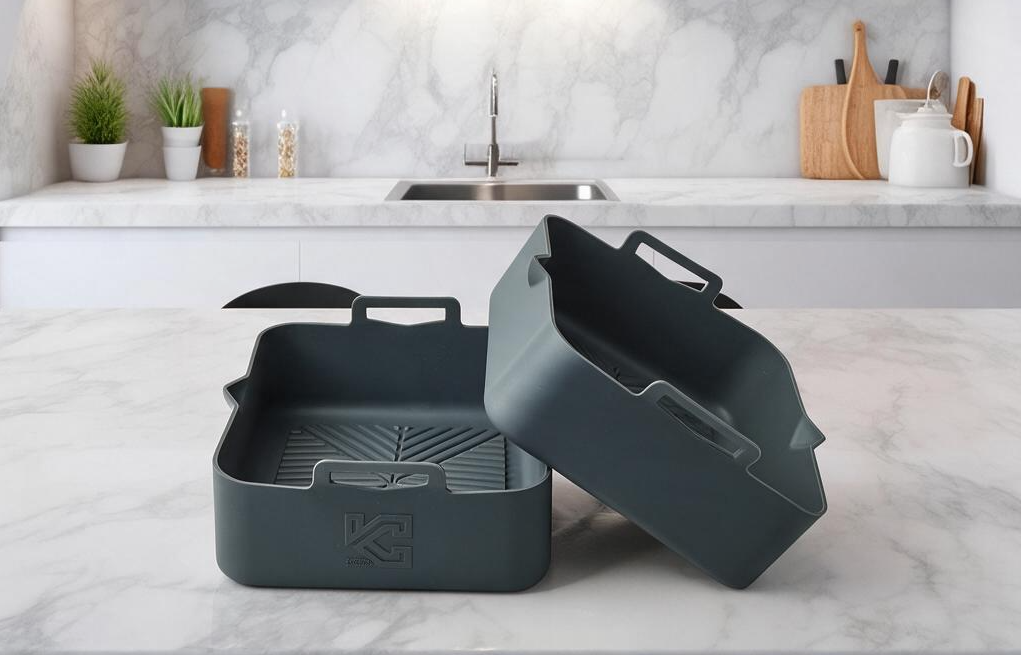 Two dark gray kitchen curated Silicone liners with handles, one standing upright and the other tilted on top, displayed on a white marble kitchen countertop with a marble backsplash in the background.